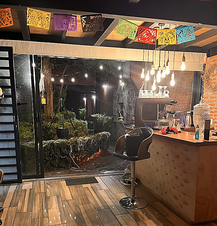 Barra de la entrada de Nails OK con papel picado de colores, focos colgantes y la puerta hacia un jardín con luces