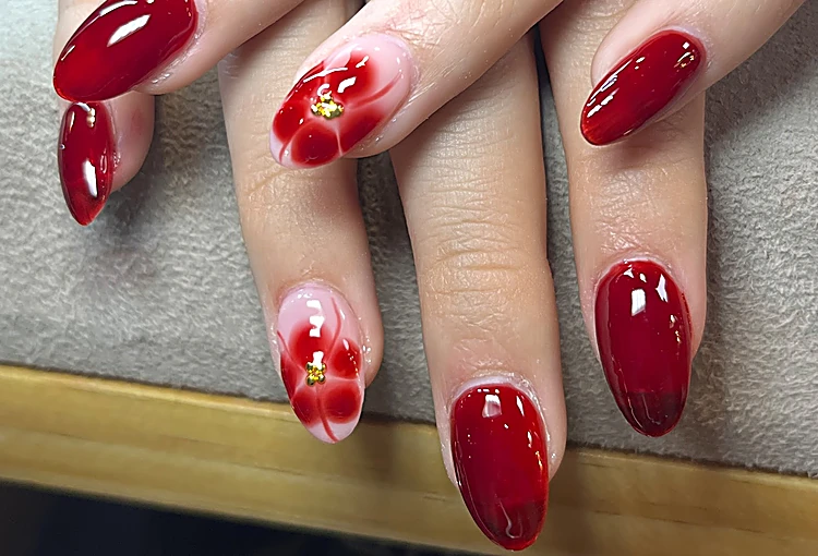 Uñas almendradas rojo intenso con una flor roja pintada en dos dedos